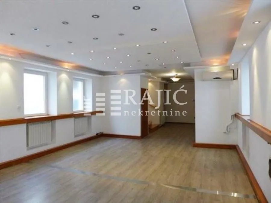 Spacious empty room with a dropped ceiling and recessed lighting.