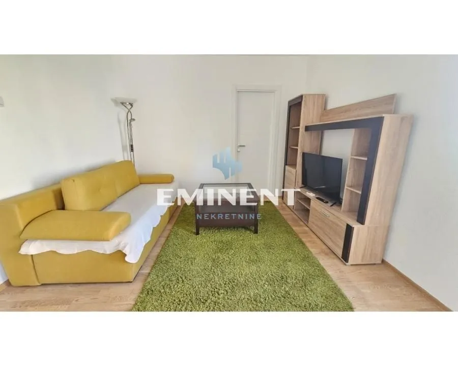 Living room with a yellow sofa, TV unit, and a rug.
