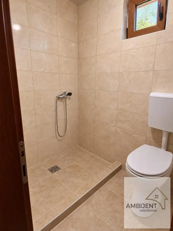 Kupatilo obloženo keramičkim pločicama sa tuš kabinom i toaletom.