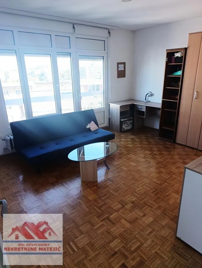 Living room with a sofa, desk, and parquet flooring.