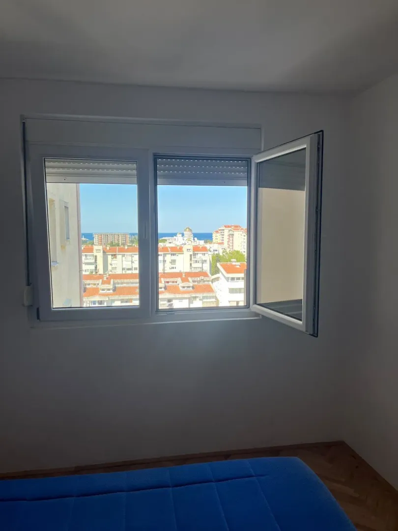 Pogled kroz prozor spavaće sobe na grad i more.