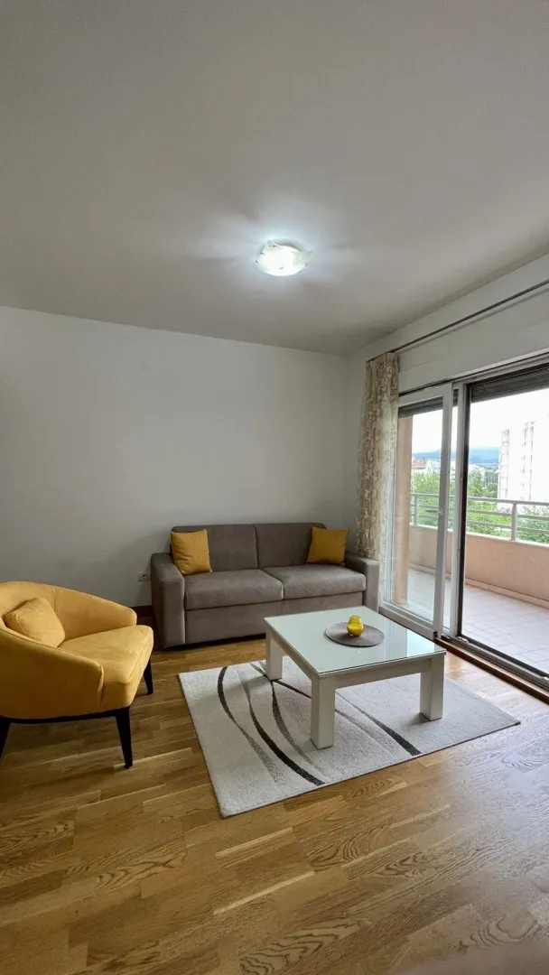 Svijetla dnevna soba sa sivim dvosjedom, žutom foteljom i izlazom na balkon.