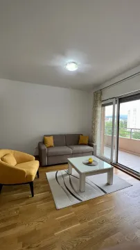 Svijetla dnevna soba sa sivim dvosjedom, žutom foteljom i izlazom na balkon. - image 3