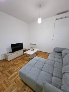 Dnevna soba sa sivom ugaonom garniturom, televizorom i parketom na podu. - image 3