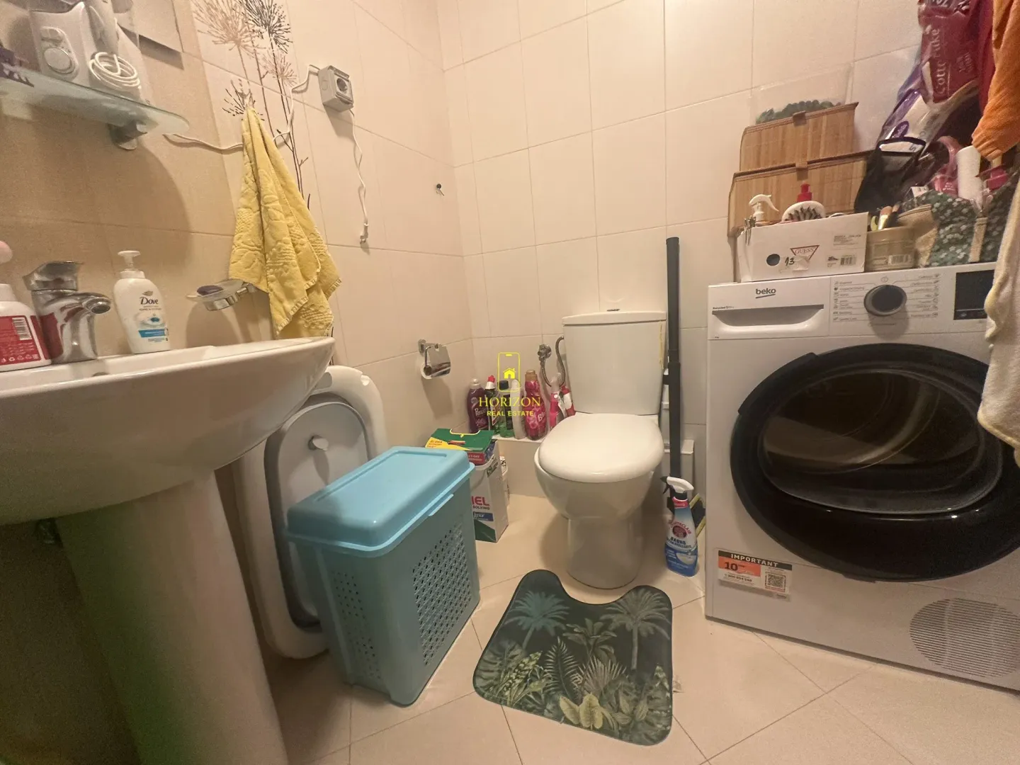 Manje uredno kupatilo sa umivaonikom, wc šoljom i veš mašinom.
