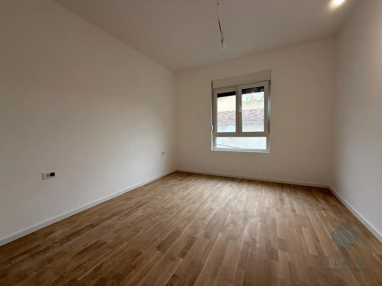 Prazna soba sa drvenim podom i jednim prozorom.