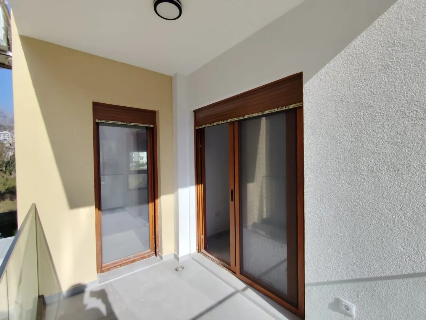Nenamješten balkon sa staklenim ogradama i drvenim balkonskim vratima.