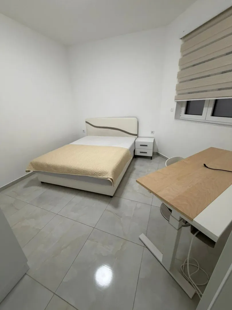 Bright and tidy bedroom with a double bed, nightstand, and a desk.