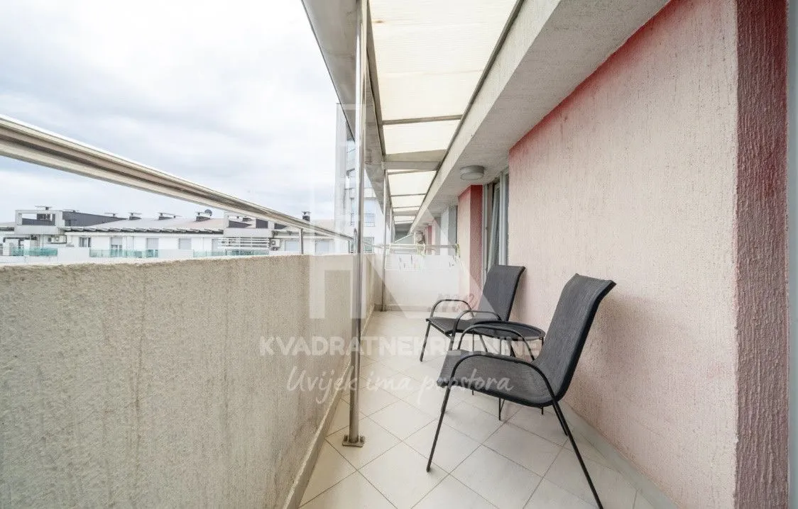 Covered balcony with chairs and a view of surrounding buildings.
