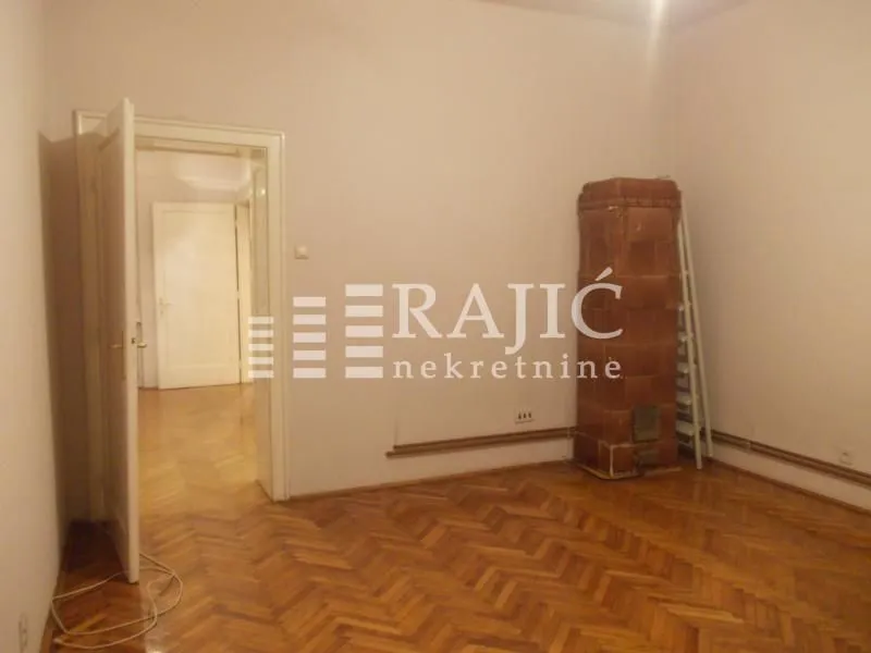 Empty room with parquet flooring and a tiled stove.