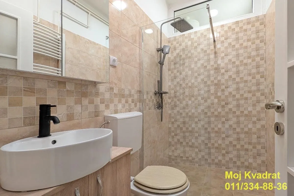 Kupatilo opremljeno umivaonikom, WC šoljom i tuš kabinom sa staklenim paravanom.