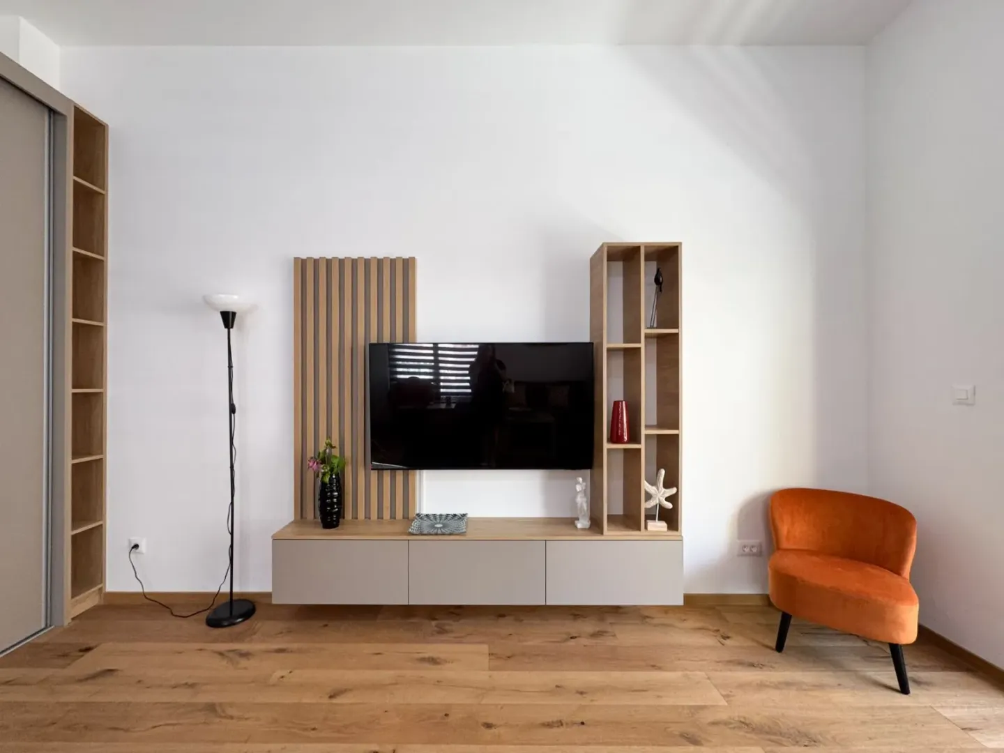 Dnevna soba sa TV komodom i narandžastom foteljom.