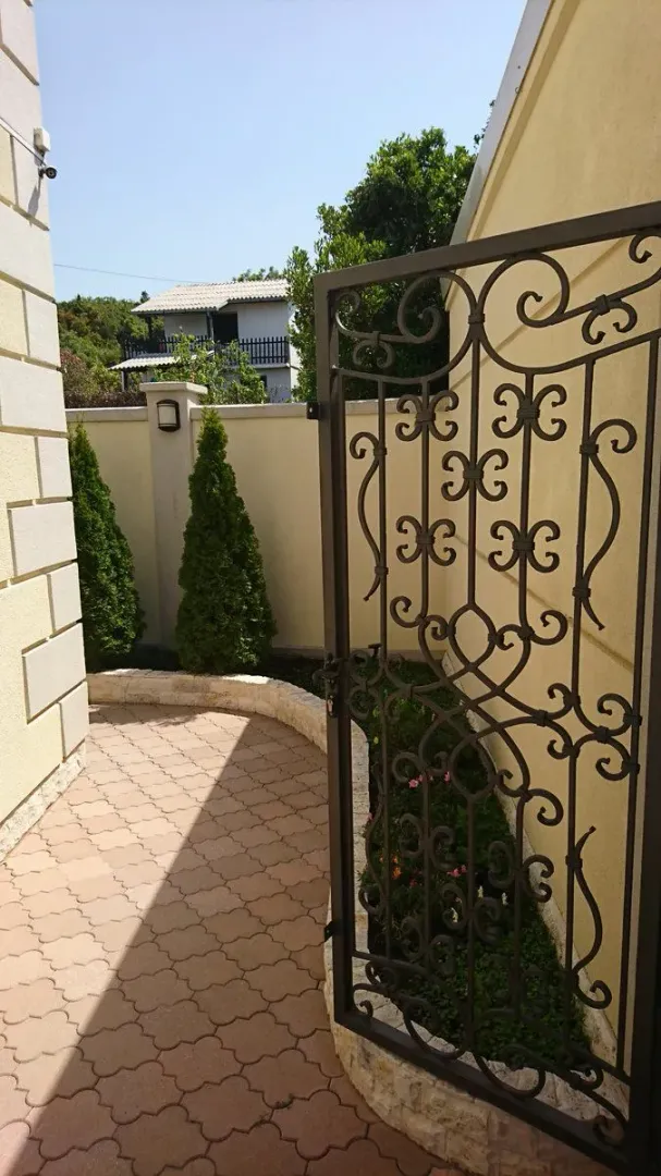 Popločana staza u dvorištu sa ukrasnom kapijom od kovanog gvožđa.