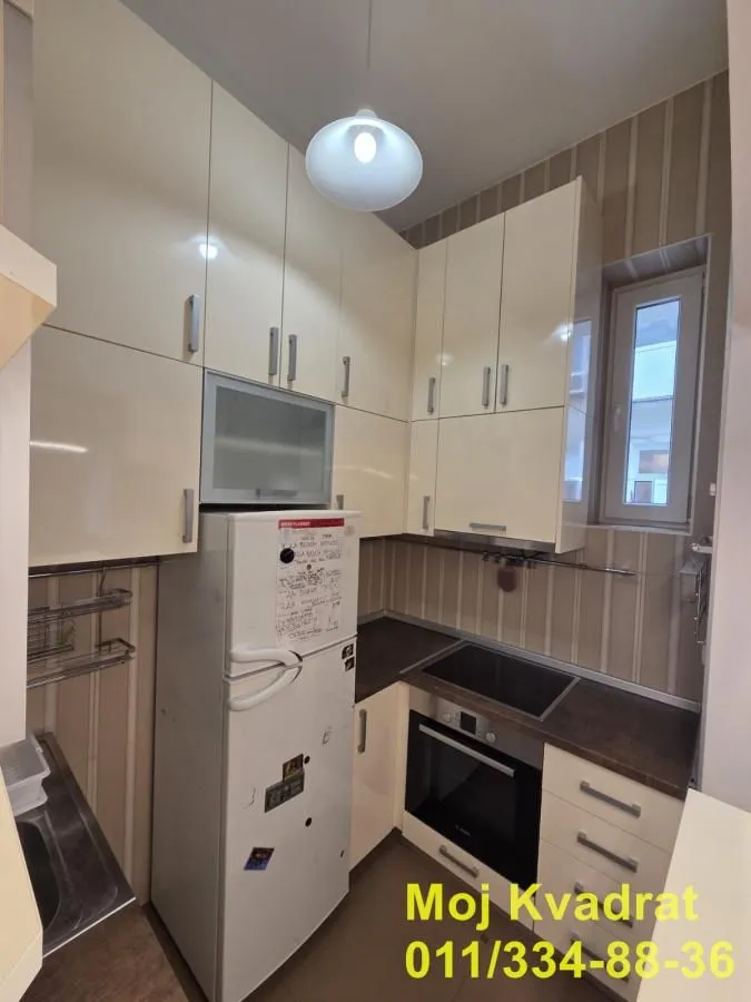 Manja kuhinja sa svetlim kuhinjskim elementima i ugrađenim kućnim aparatima.