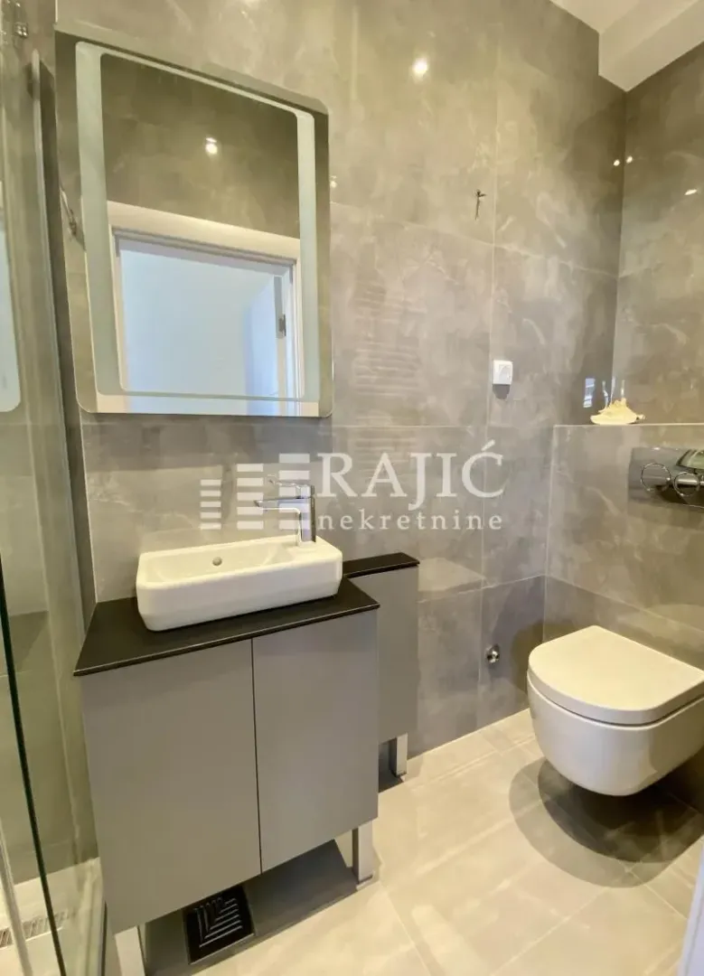 A modern equipped bathroom with a washbasin and toilet clad in ceramic tiles.