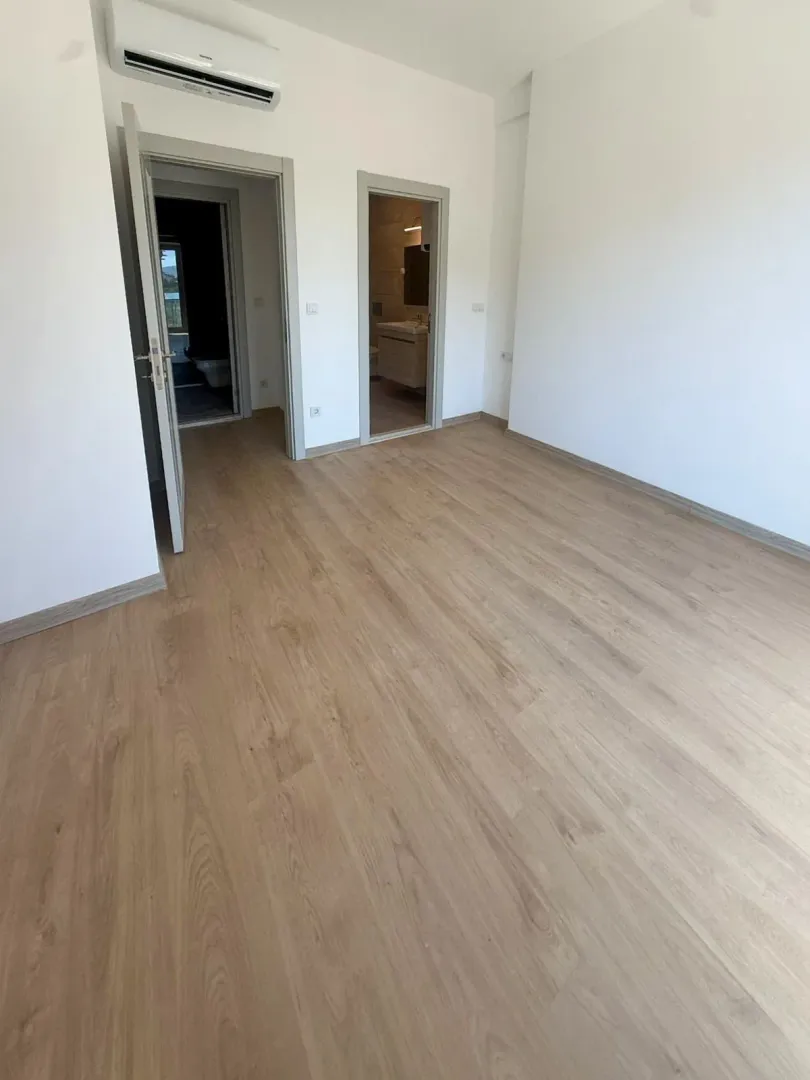 Prazna soba sa laminatom, klima uređajem i vratima koja vode u druge prostorije.