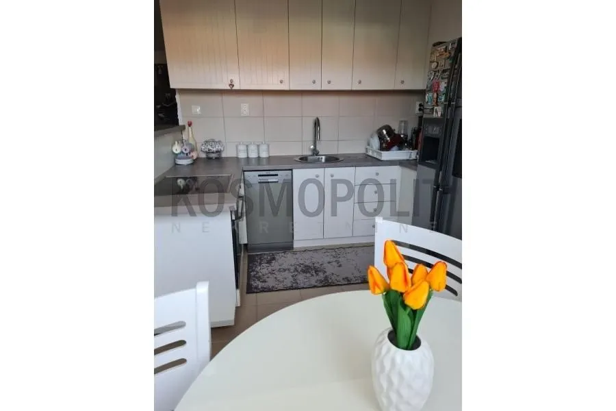 Kuhinja sa belim elementima i trpezarijskim stolom u prvom planu.
