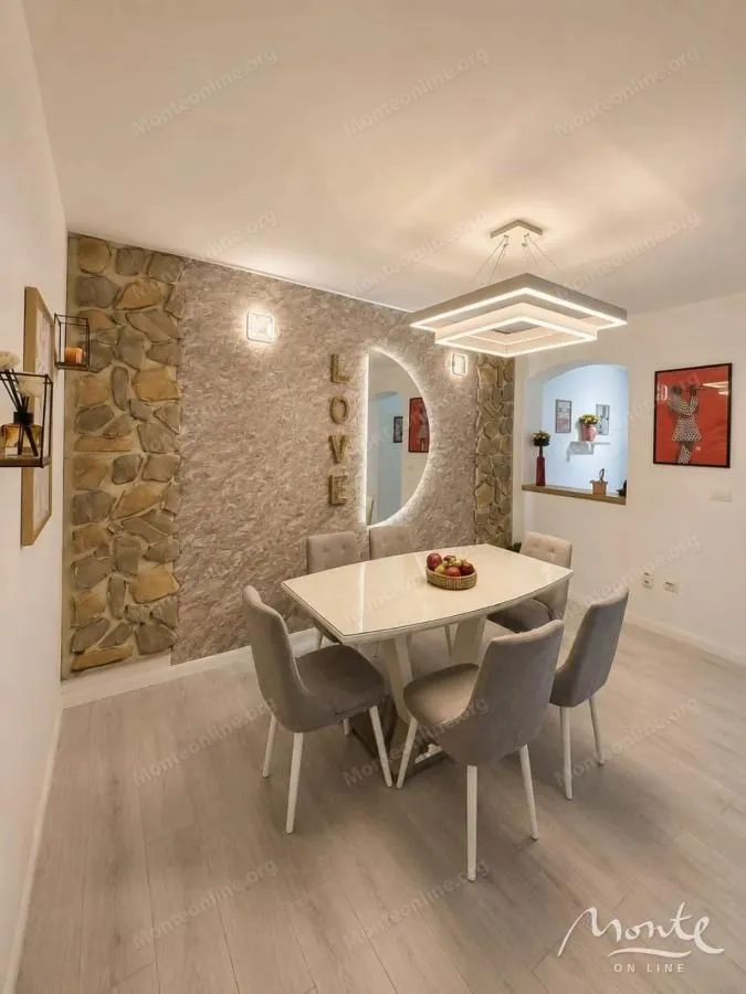 Trpezarija sa modernim stolom, stolicama i dekorativnim zidom od kamena.
