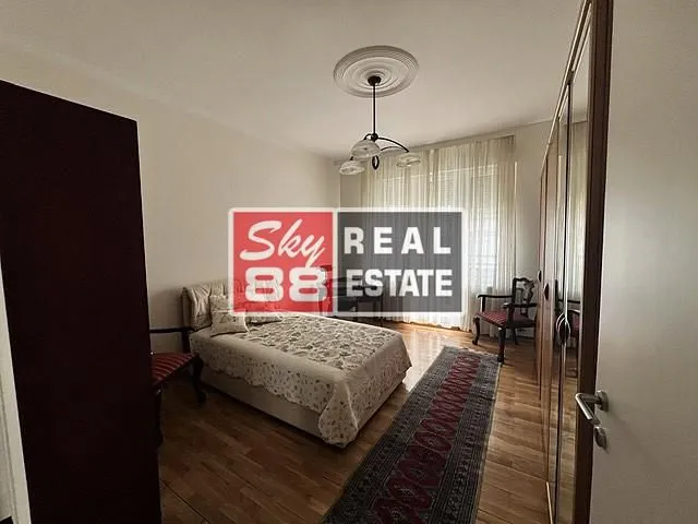Nameštena spavaća soba sa bračnim krevetom, ormarom i drvenim podom.