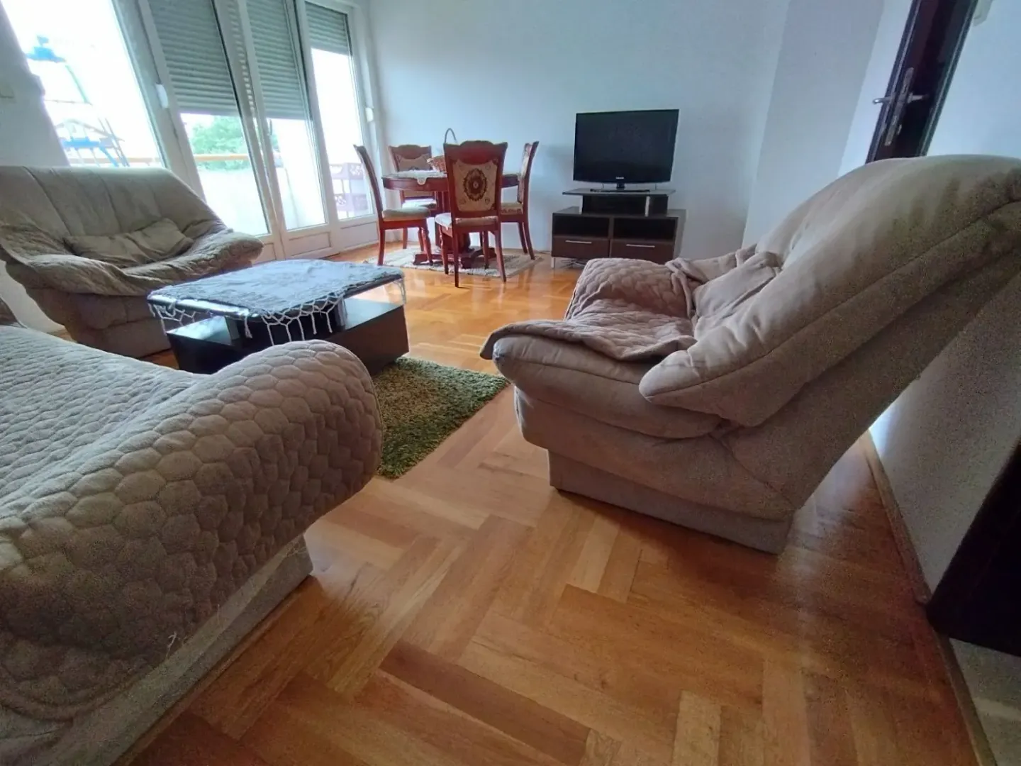 Dnevna soba sa udobnim foteljama, televizorom i trpezarijskim stolom u pozadini.