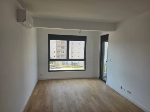 Prazna soba sa parketom, klima uređajem i pogledom na zgrade kroz prozor. - image 5