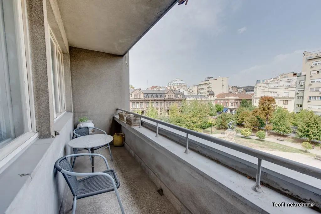 Natkriveni balkon sa stolom, stolicama i pogledom na park i grad.