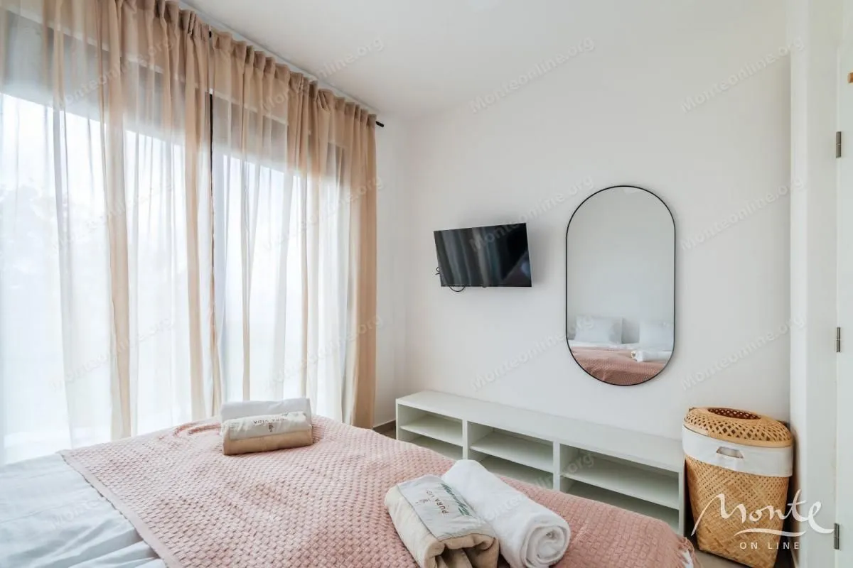Svijetla spavaća soba sa bračnim krevetom, TV-om i zavjesama.