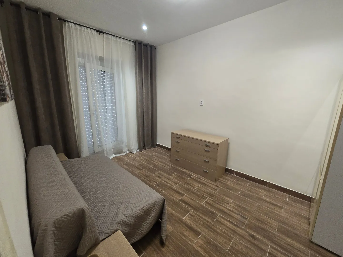 Spavaća soba sa krevetom, komodom i prozorom sa zavjesama.