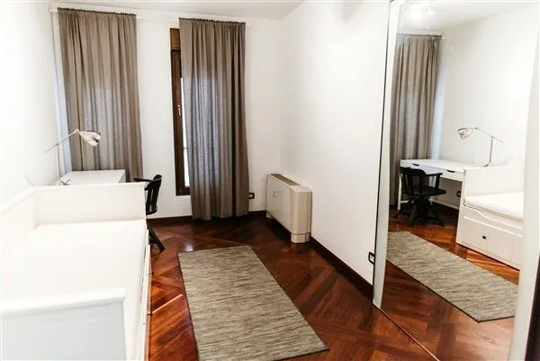 Bright bedroom with a single bed, a study desk, and a large mirror.