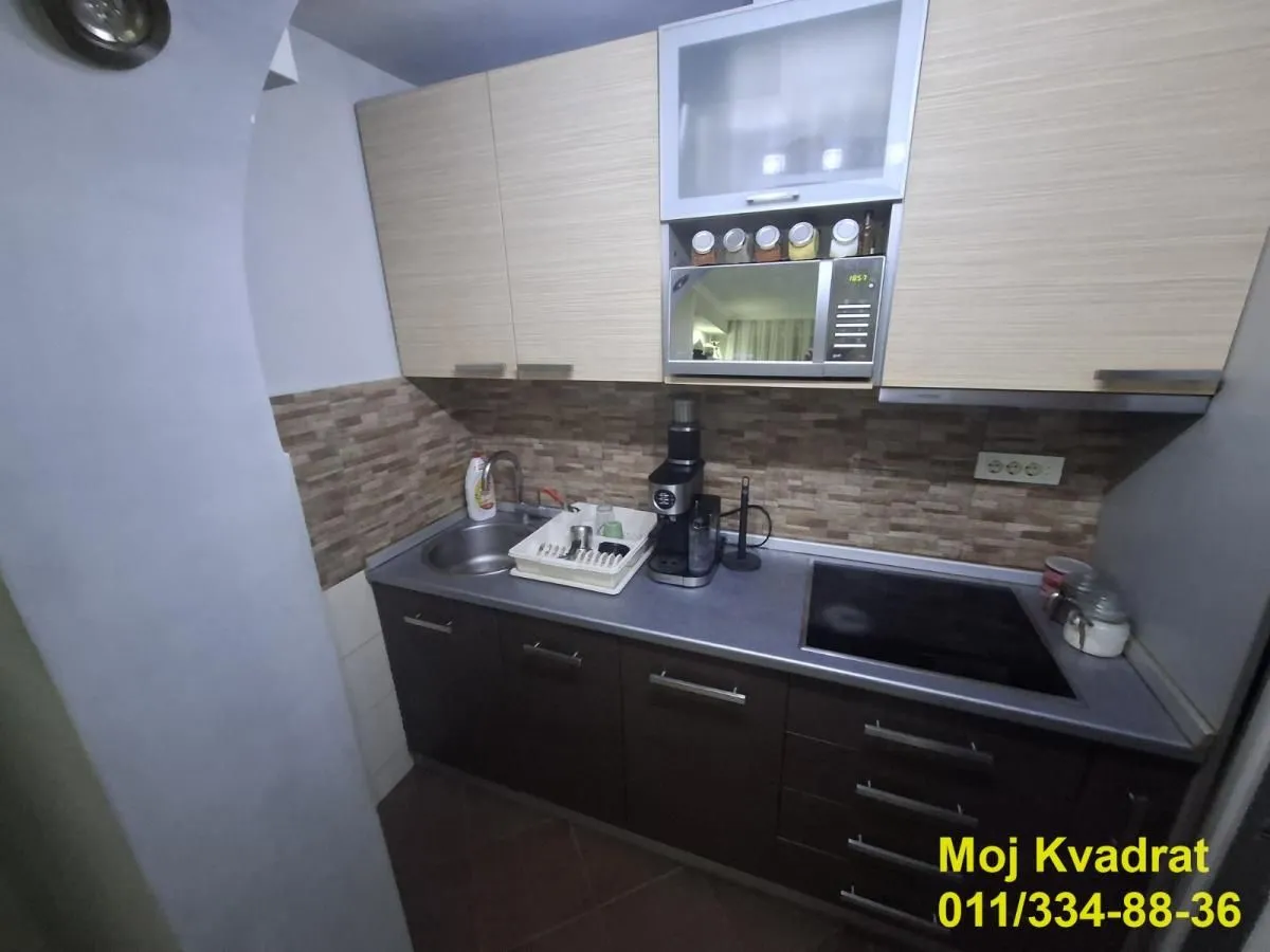 Manja kuhinja sa donjim i gornjim kuhinjskim elementima i ugrađenom pločom za kuvanje.