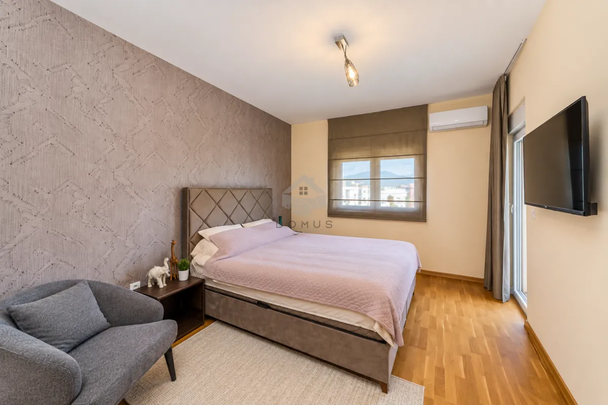Furnished bedroom with a double bed, an armchair, and a wall-mounted TV.