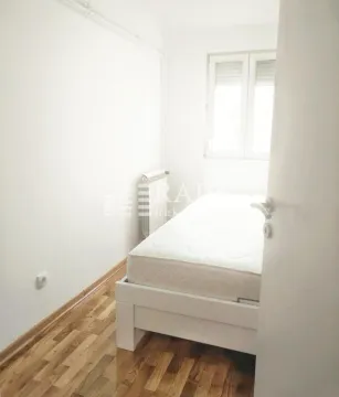 Manja spavaća soba sa belim krevetom i drvenim podom. - image 9