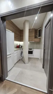 Pogled iz hodnika na opremljenu kuhinju sa belim elementima i drvenim detaljima. - image 7