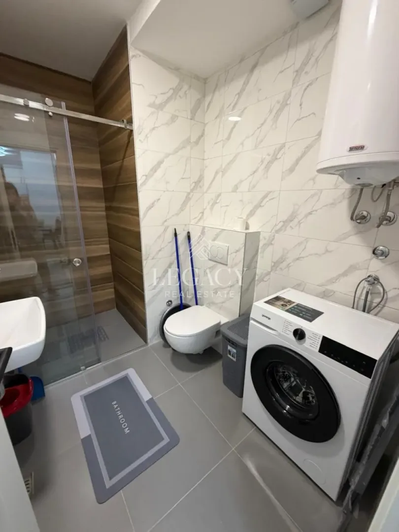 Modern bathroom equipped with a shower cabin, sink, toilet, and washing machine.