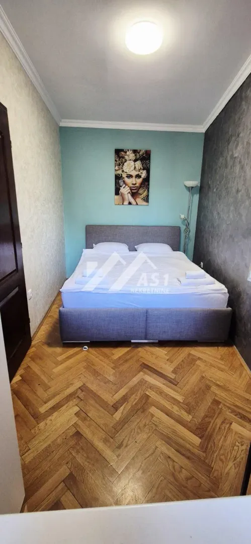 Spavaća soba sa bračnim krevetom i parketom na podu.