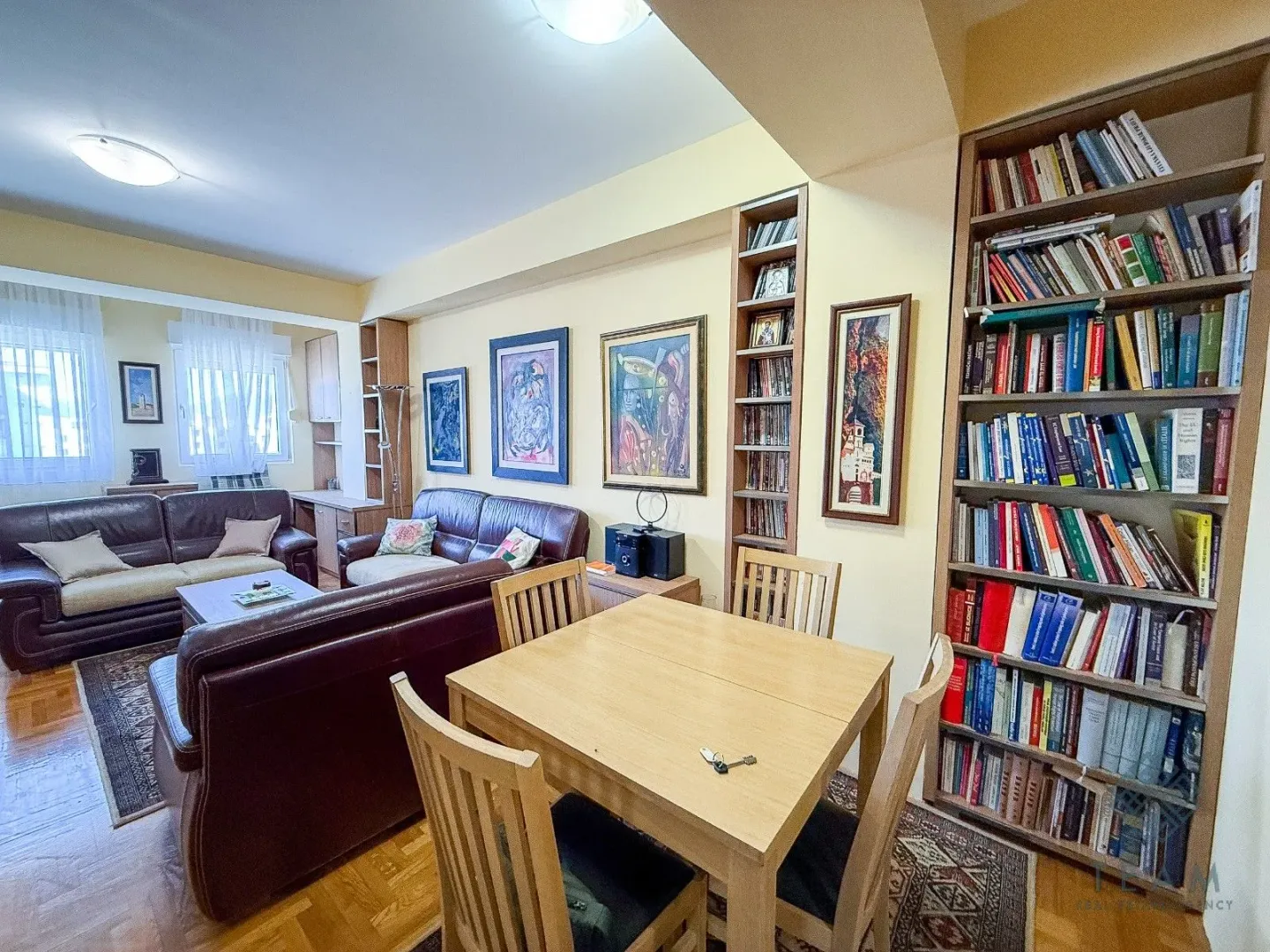 Living room with seating furniture, a dining table and a large bookshelf.