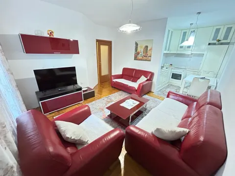Dnevna soba sa crvenim kožnim garniturama, televizorom i pogledom na kuhinju u pozadini. - image 11