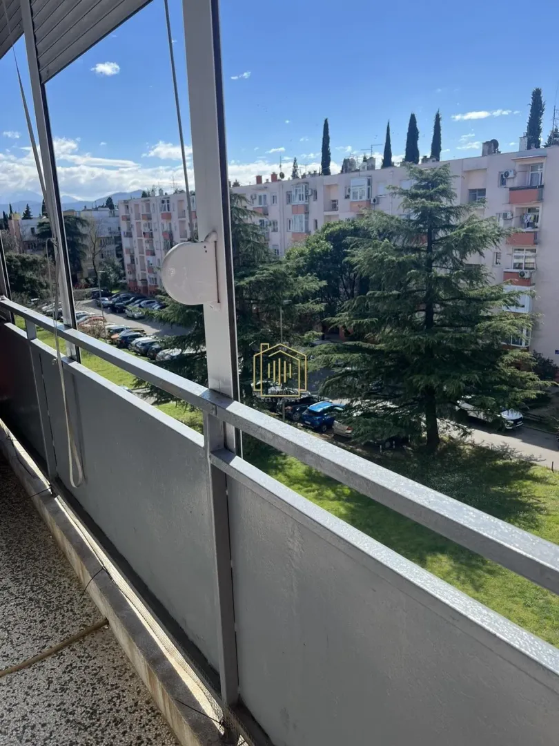 Pogled sa balkona na okolne zgrade i zelenu površinu.