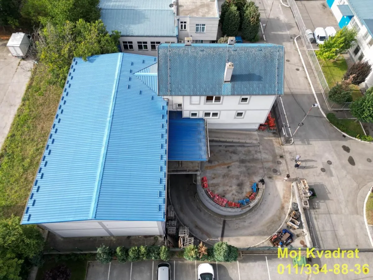 Aerial view of a commercial building with a blue roof and accompanying yard.