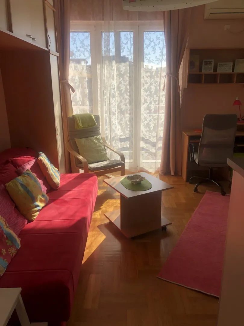 Bright living room with a red sofa and a study desk by the window.
