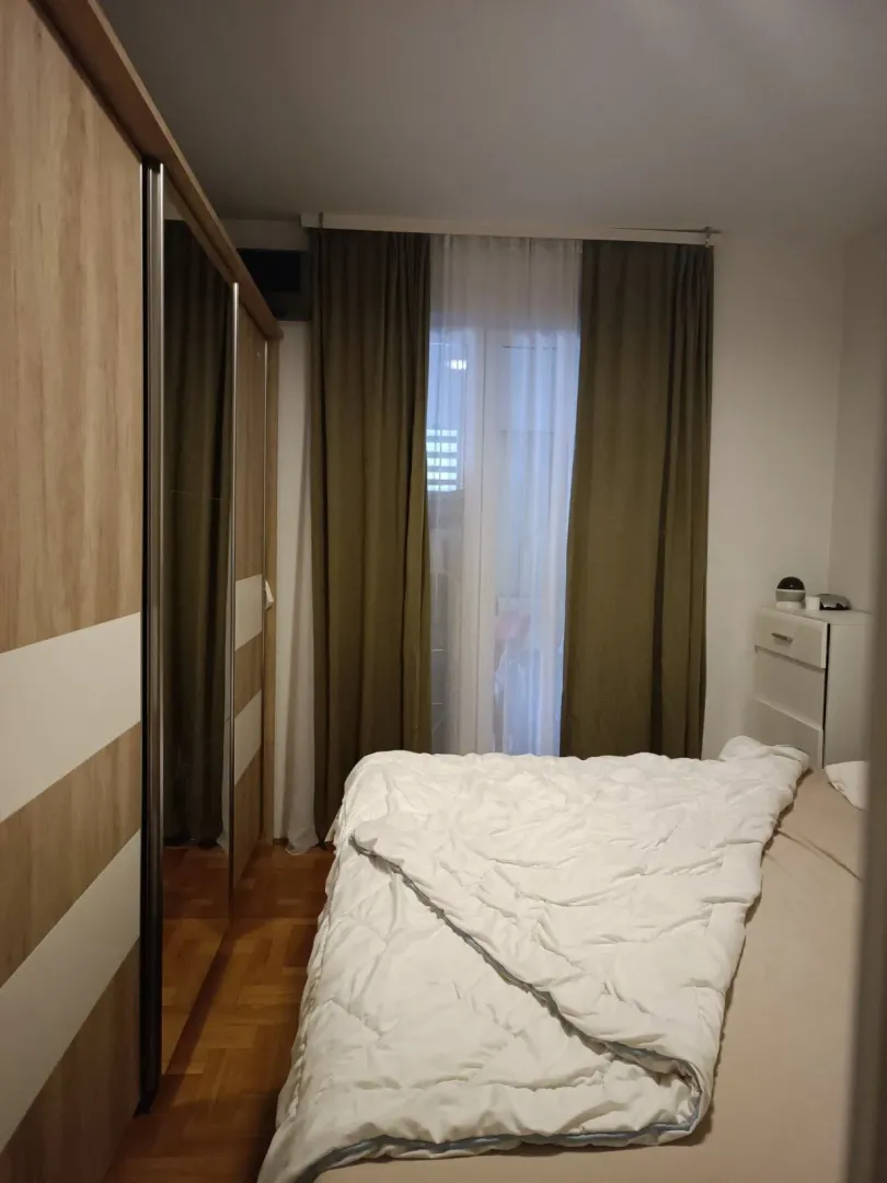 Namještena spavaća soba sa bračnim krevetom, garderoberom i balkonskim vratima.