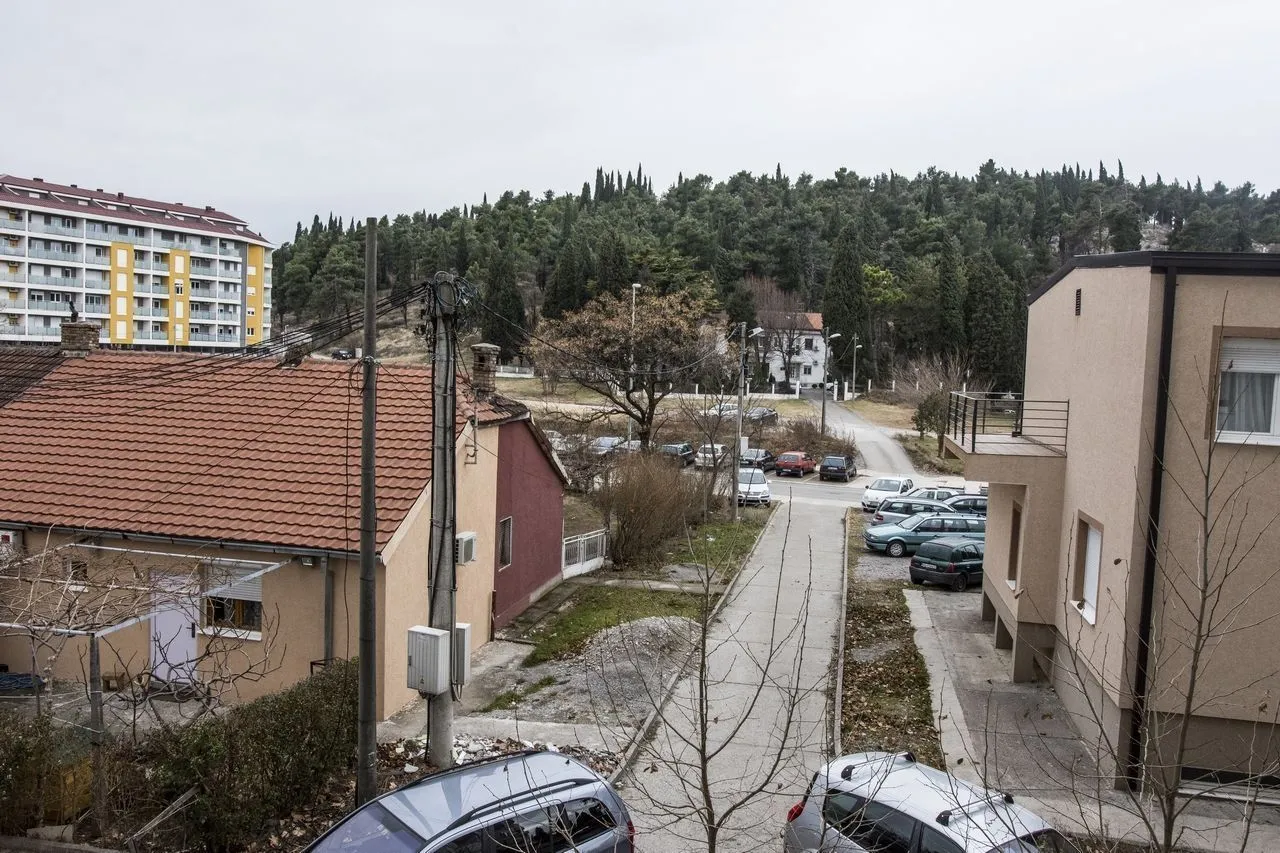 Pogled sa prozora na okolno naselje i brdo sa drvećem.