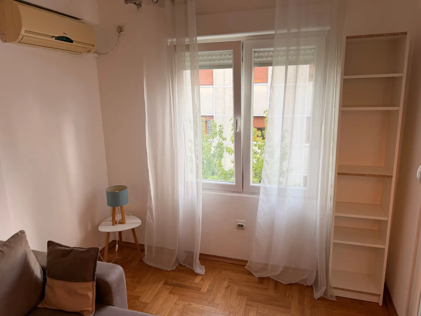 Living room with a sofa, bookshelf, and a window with white curtains.