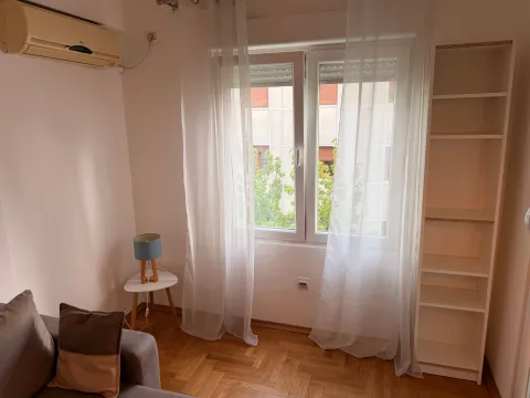 Living room with a sofa, bookshelf, and a window with white curtains. - image 4