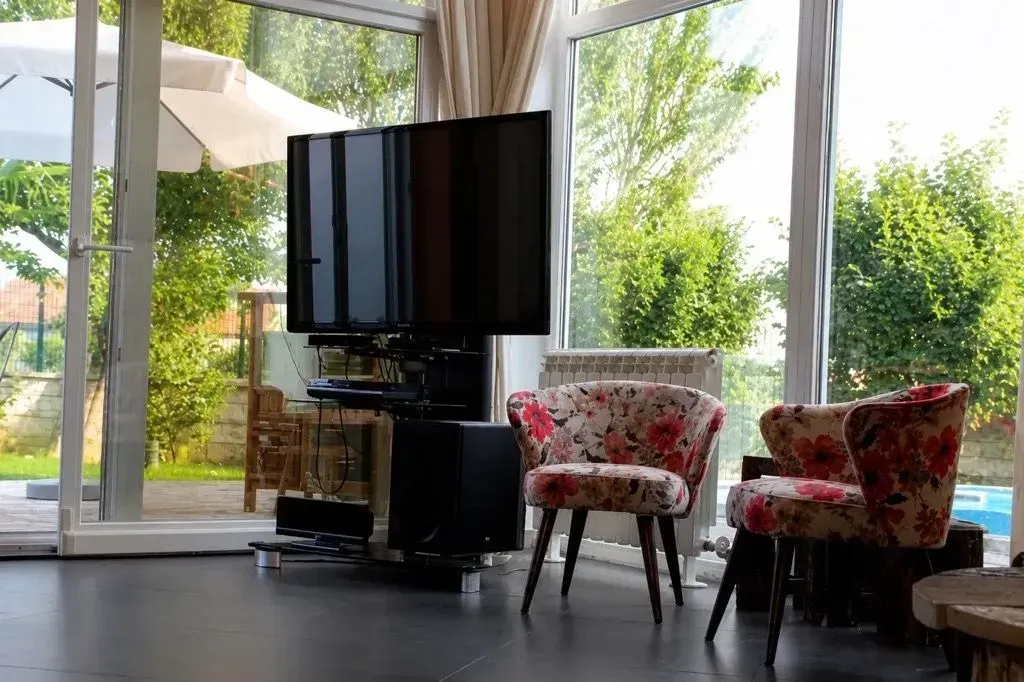 Bright living room with large windows, television, and armchairs.