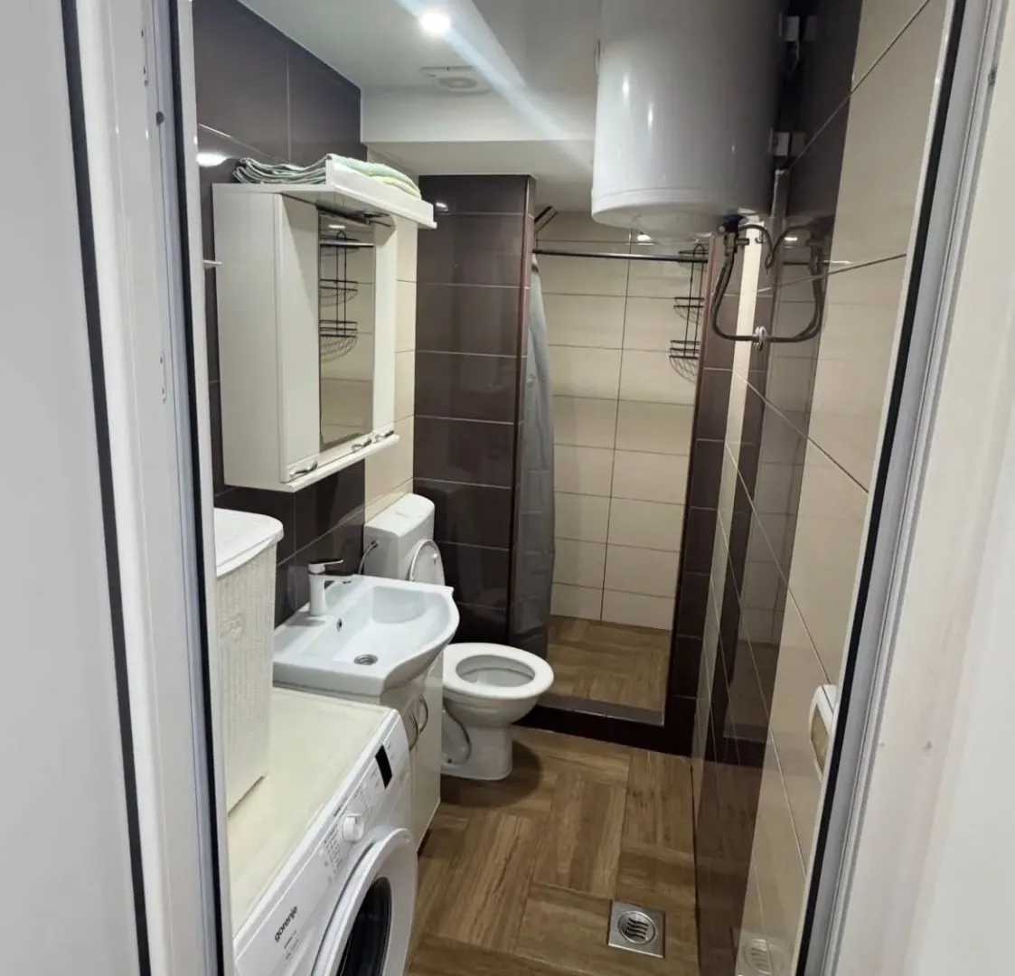 Smaller bathroom with a shower cabin, sink, toilet, and washing machine.