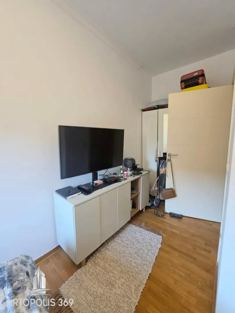 Dnevna soba sa televizorom na komodi i ormarom u uglu.