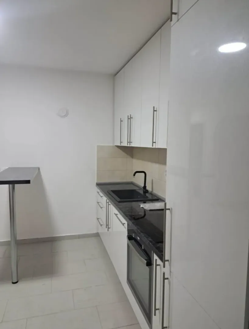 Manja bijela kuhinja sa tamnom radnom pločom i šankom.