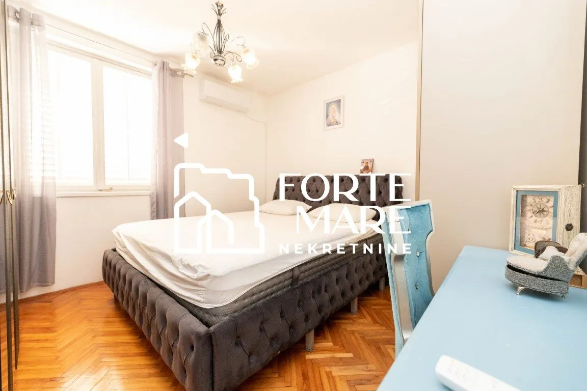 Spavaća soba sa bračnim krevetom, plavim radnim stolom i parketom.
