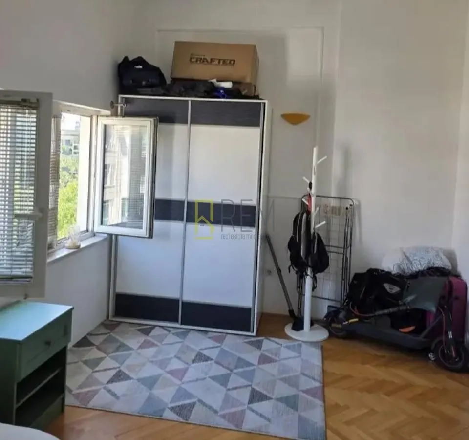 Manja soba sa ormarom, tepihom i otvorenim prozorom.